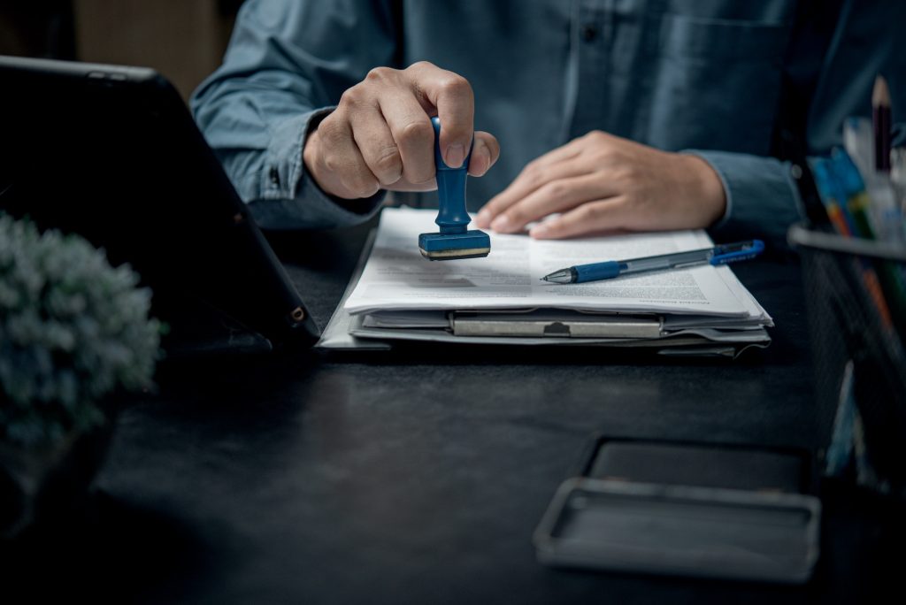 hand stamping with approved stamp on certificate document Contract Form Paper at desk,